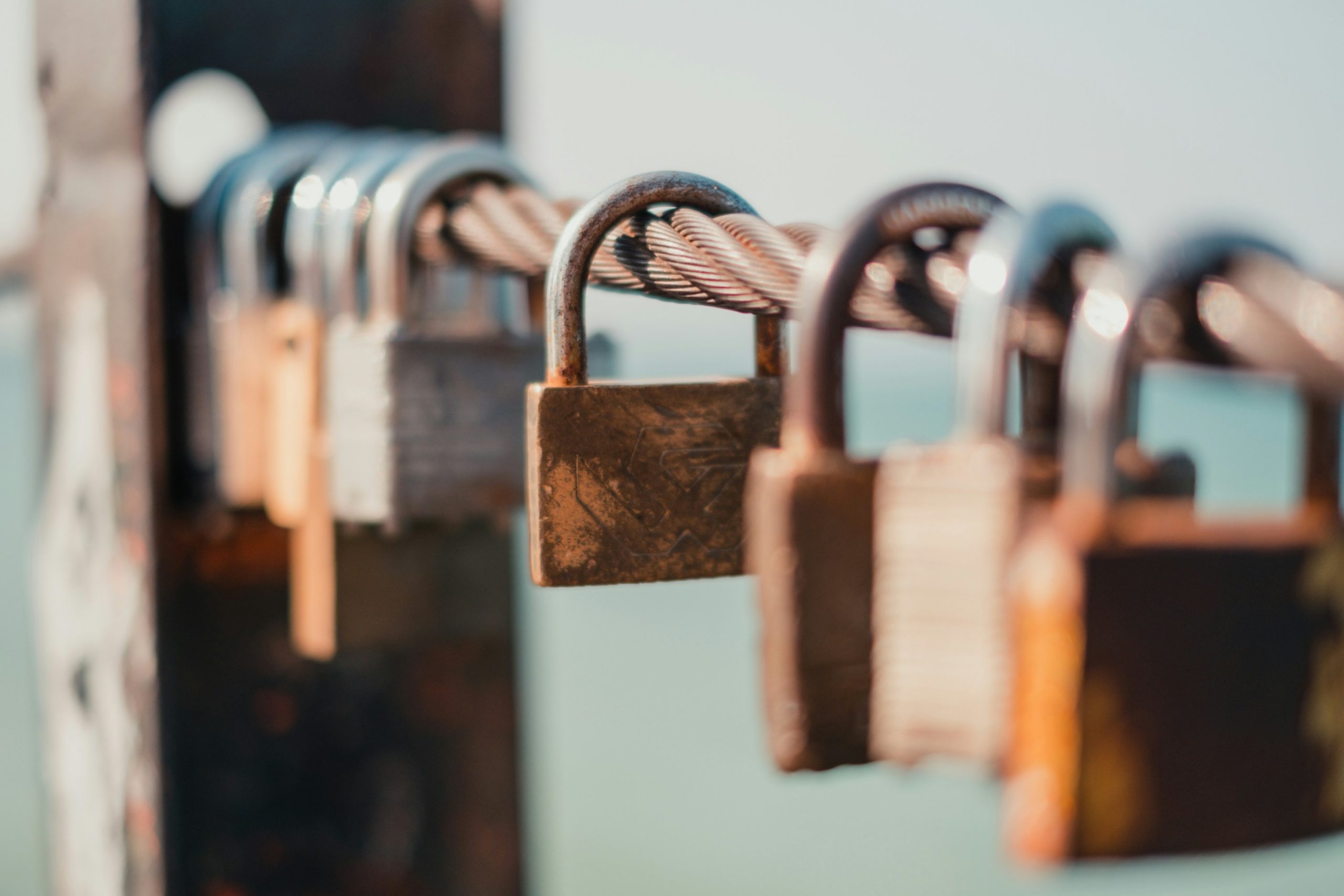 Une rangée de cadenas rouillés suspendus à un câble métallique, avec un fond flou et un ciel bleu clair.