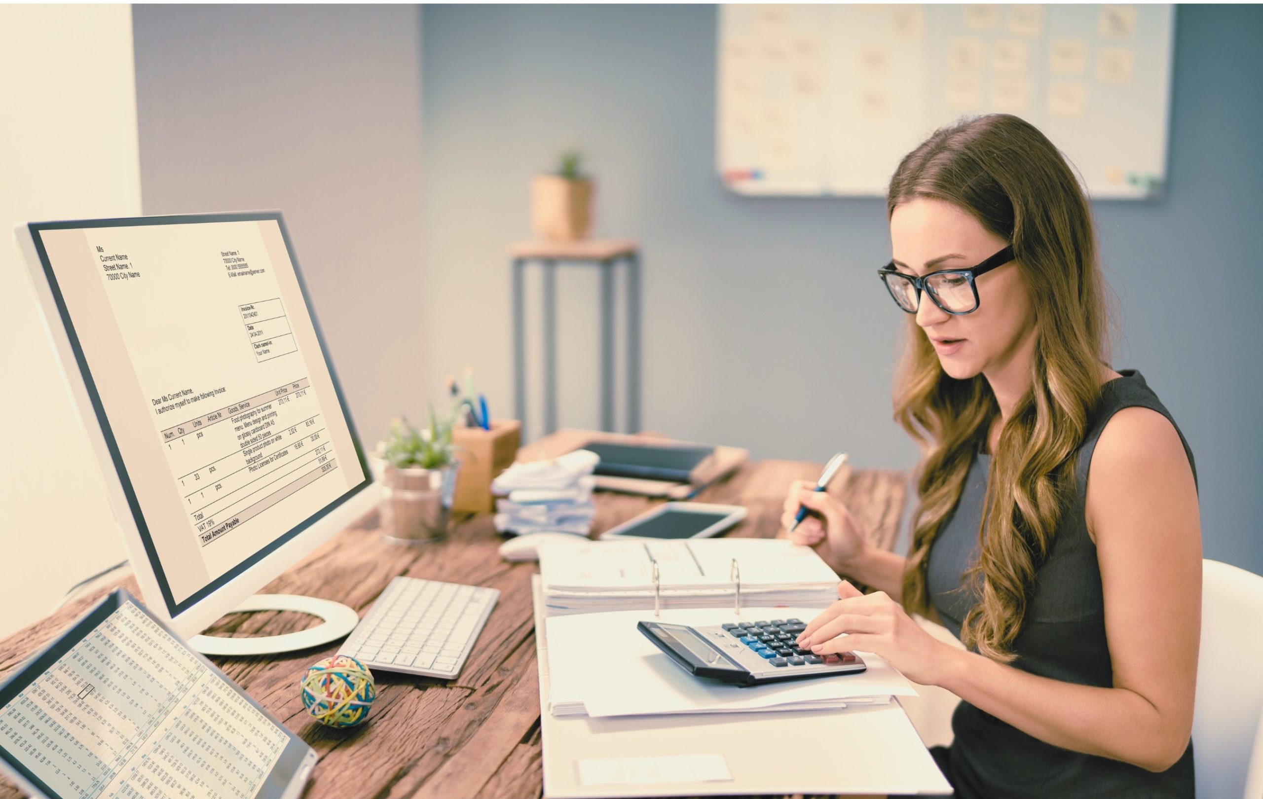 Femme travaillant sur un bureau avec une calculatrice et des documents financiers, face à un écran affichant une facture.@AndreyPopov_Getty