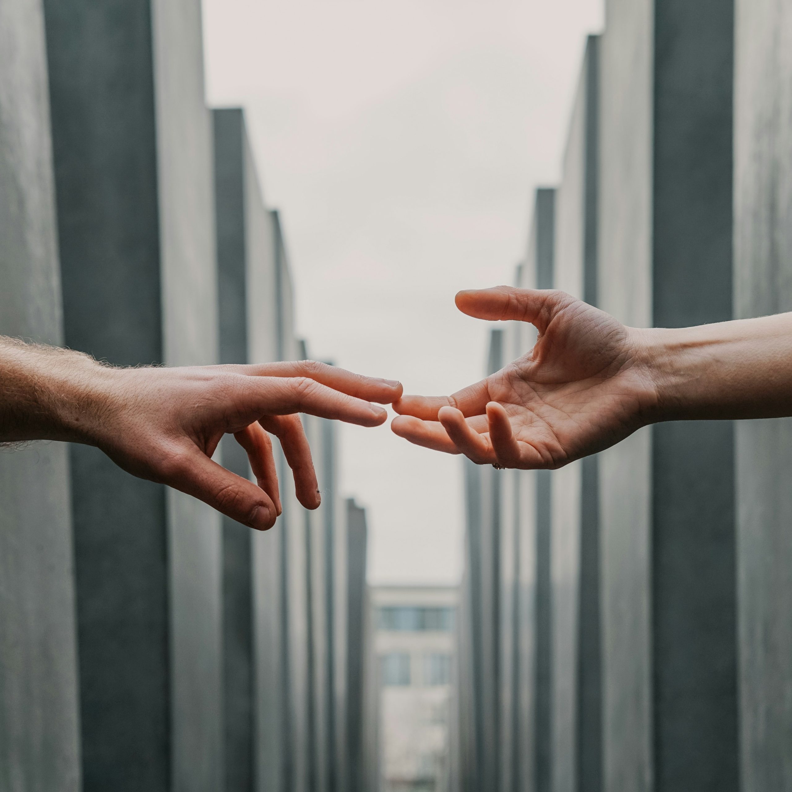 Deux mains tendues l’une vers l’autre, prêtes à se toucher au milieu d’un espace architectural aux lignes géométriques.