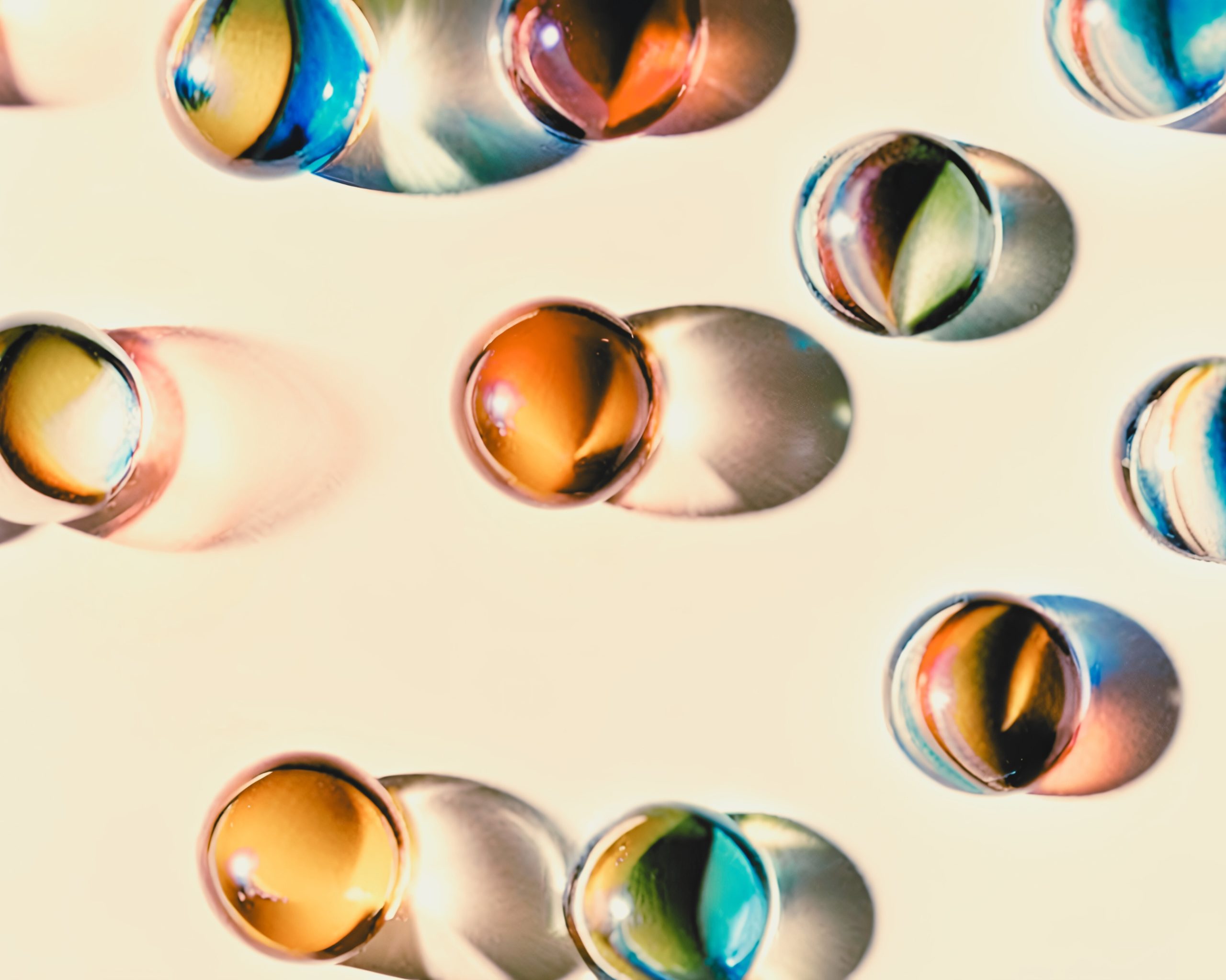 Billes colorées en verre projetant des ombres multicolores sur une surface claire.