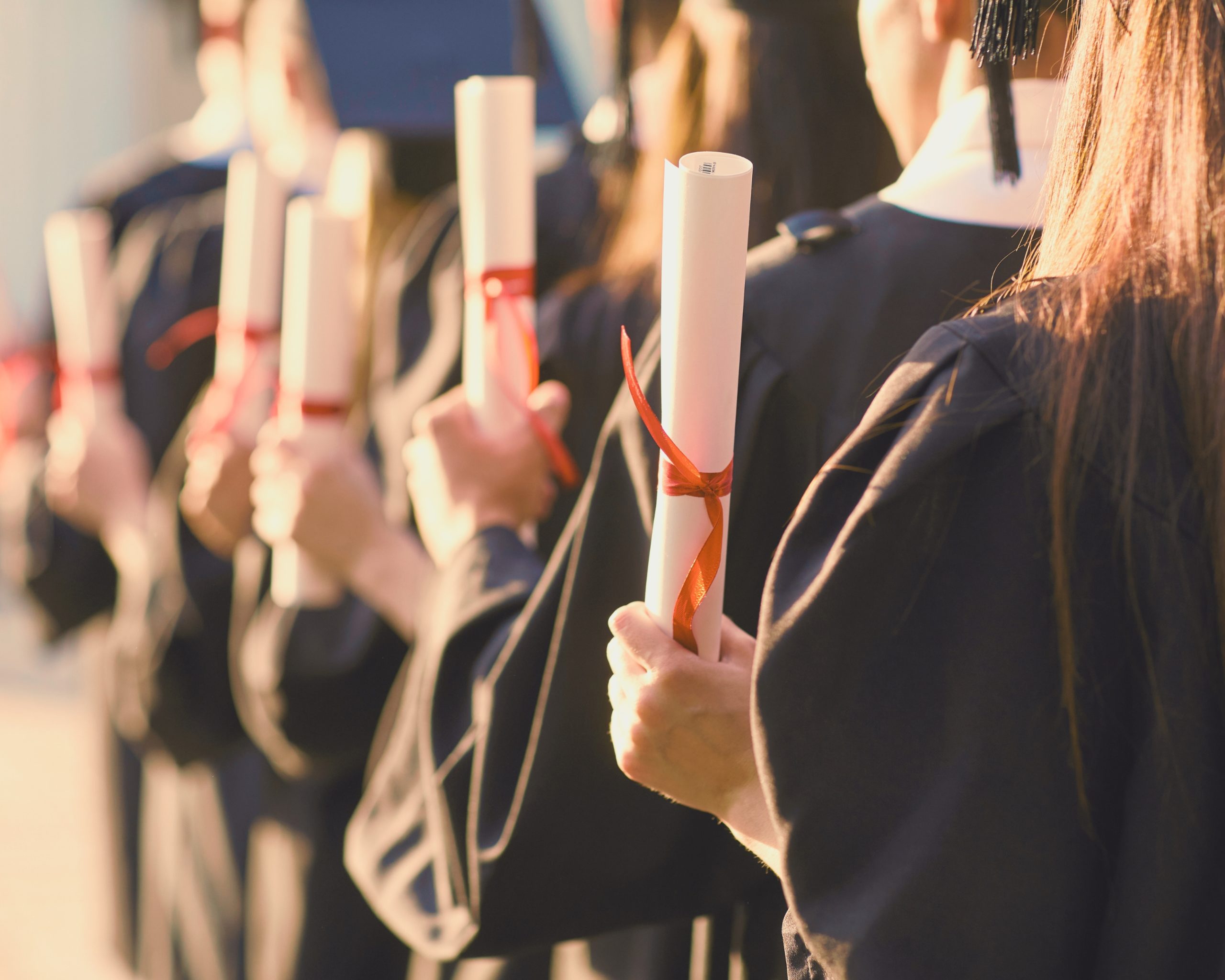 Groupe d’étudiants en toge de fin d’études tenant leur diplôme roulé, noué d’un ruban rouge.
