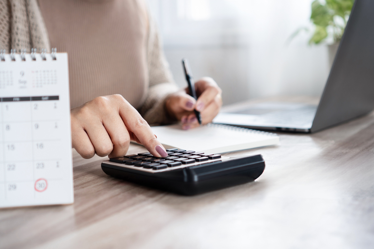 Femme dans son bureau qui appuie sur une calculatrice et prend des notes